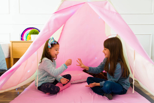 Excited little girls friends laughing having fun while playing games doing hand gestures inside a pink teepee - Photo, Image