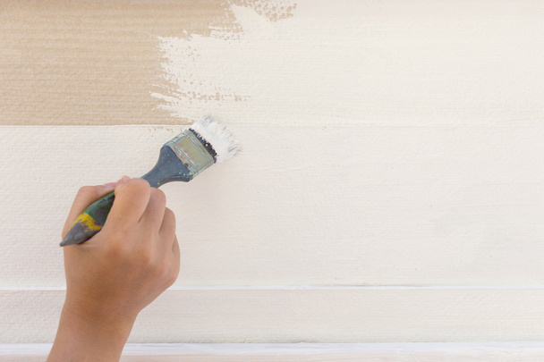 εργαζόμενος χέρι, κρατώντας τη ζωγραφική με το πινέλο λευκό σε ξύλινο φράχτη - Φωτογραφία, εικόνα
