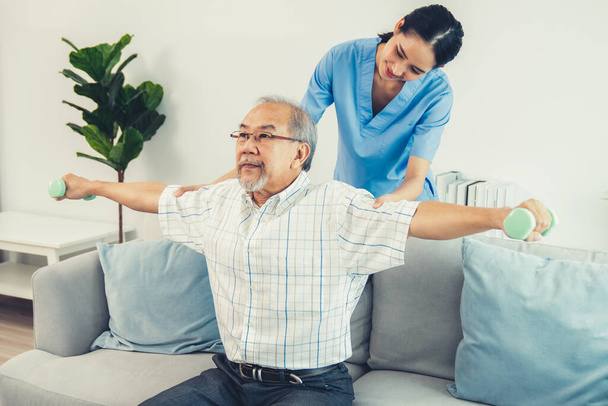 Contented senior patient doing physical therapy with the help of his caregiver. Senior physical therapy, physiotherapy treatment, nursing home for the elderly - 写真・画像