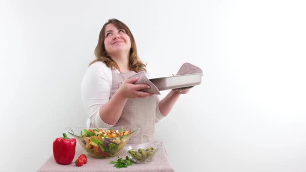middle-aged woman housewife cook holding tray of food in hands sniffs it smiling showing tasty dance shakes head In foreground vegetables salad ingredients for dinner or lunch at end shows thumbs up - Video