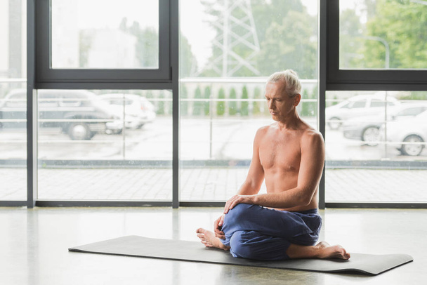 barefoot man in blue pants sitting in twisting yoga pose on mat - Photo, Image