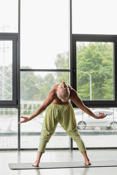 full length of shirtless man in green pants doing backside bend in yoga studio  - Valokuva, kuva
