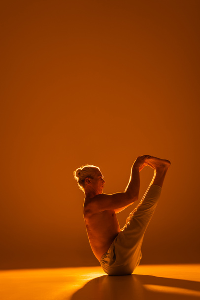 longitud completa de hombre sin camisa haciendo barco yoga pose en marrón   - Foto, imagen