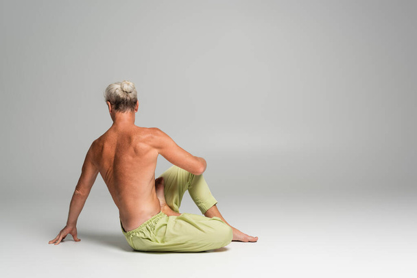 back view of shirtless man doing supine spinal twist yoga pose on grey background  - Foto, Imagen