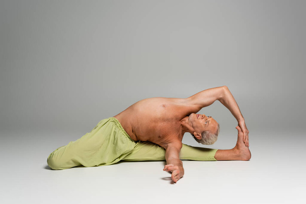 hombre sin camisa en pantalones haciendo sentado puerta yoga pose sobre fondo gris  - Foto, imagen