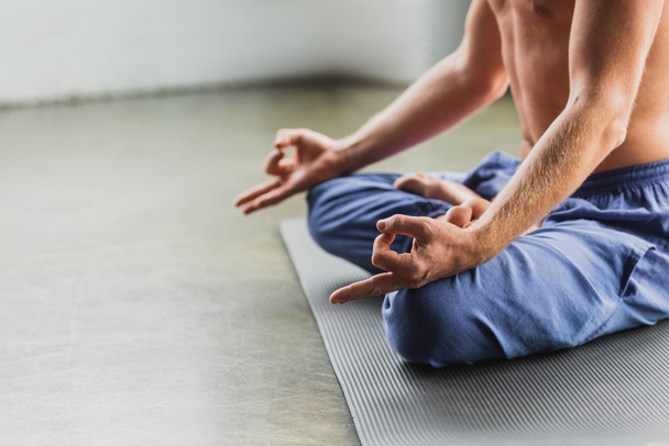 partial view of man in blue pants sitting in lotus pose and doing gyan mudra  - Φωτογραφία, εικόνα