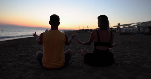Пара йоги для медитації та медитації під час безтурботного заходу сонця на пляжі. Дівчина і чоловік розслабляються в положенні лотоса в спокійний момент дзен
 - Кадри, відео