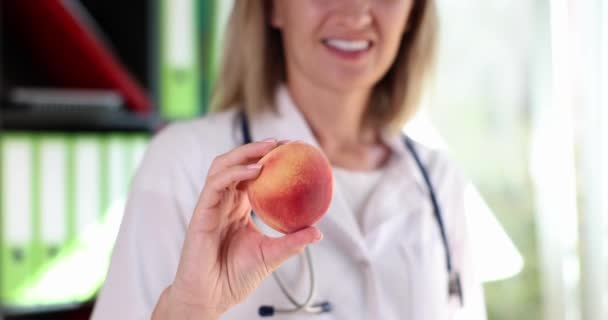 Woman doctor nutritionist therapist offering fresh peach. Vitamins healthy food and diet - Video, Çekim