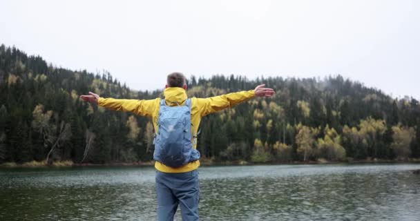 Free male tourist with outstretched arms on the shore of lake. Adventure outdoor freedom and hiking - Filmagem, Vídeo