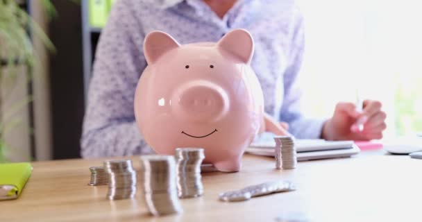 Woman counts financial savings on calculator with piggy bank. Control of expenses and cash income - Imágenes, Vídeo