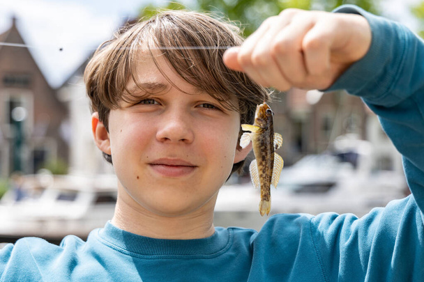 The boy caught a goby fishs on a canal in the city of Amsterdam - Фото, изображение