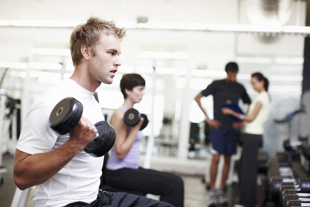 Construyendo sus bíceps. un joven guapo haciendo ejercicio con pesas en el gimnasio - Foto, imagen