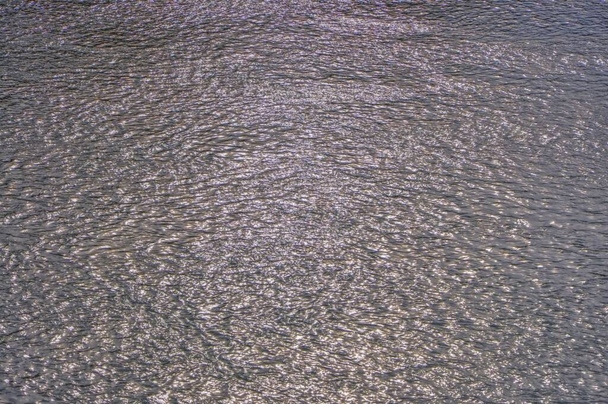 Abstract metallic color of water surface.Sea surface covered with tiny choppy waves reflecting silver light. Aerial view to deep grey water in river with sunlight. - Photo, Image