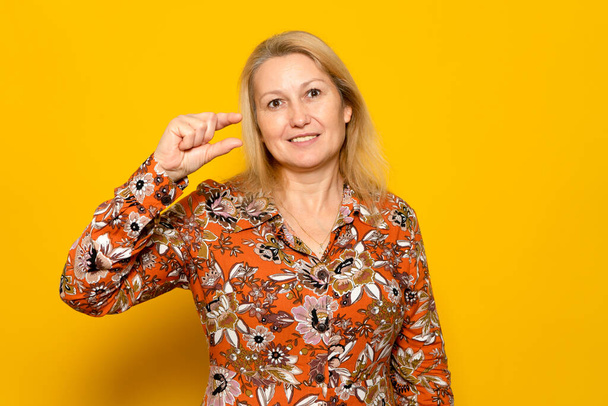 Displeased skeptical woman in print dress gesturing small, undersized, dissatisfied with low rating. Isolated on yellow background - Foto, imagen