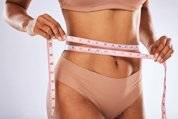 Measuring tape, stomach and woman in studio for wellness, weight loss and tummy tuck on grey background. Belly, measurement and girl model checking for progress, slimming and size after detox or diet. - Fotoğraf, Görsel