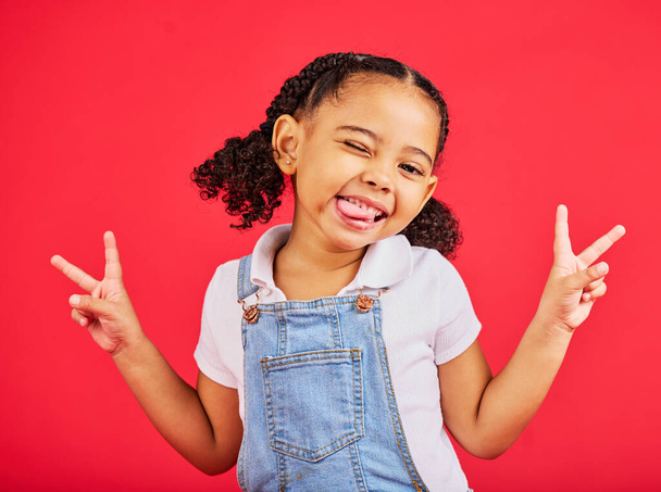 Happy, peace sign and wink with portrait of girl for summer, happiness and funny face. Meme, fashion and smile with child and hand gesture for youth, comedy and positive in red background studio. - Foto, Imagen