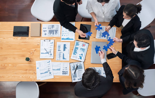 Top view businesspeople and colleagues in formal wear putting jigsaw puzzles together over meeting table with financial report papers in harmony office for team building concept. - Foto, imagen