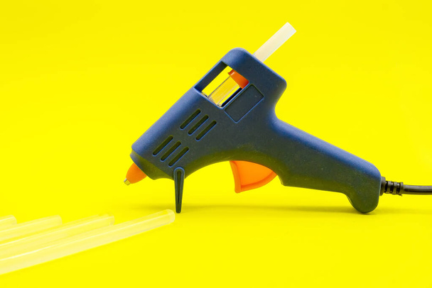 blue glue gun with silicone sticks on a yellow background. Close-up. Empty space for text. Side view - Fotó, kép