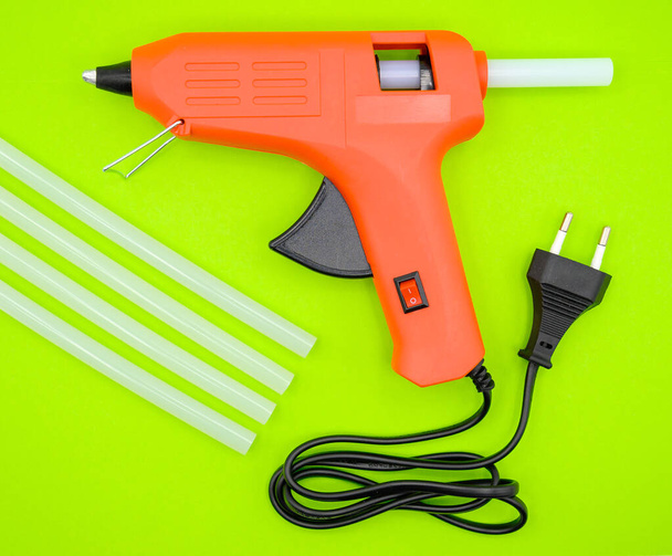 red glue gun with silicone sticks on a green background. Close-up Top view. - Foto, afbeelding