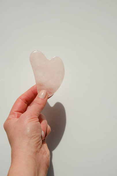 gua sha scraper made of rose quartz in a female hand.beauty devices.Gua sha facial massage device.Roller massager made of pink natural stone - Photo, Image