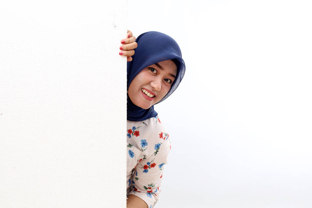Funny and happy asian muslim woman peeking behind the wall. Isolated on white background - Foto, imagen