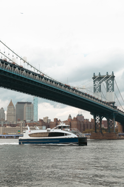 Modernes Boot unter Manhattan Brücke in der Nähe von Wolkenkratzern von New York City im Hintergrund - Foto, Bild