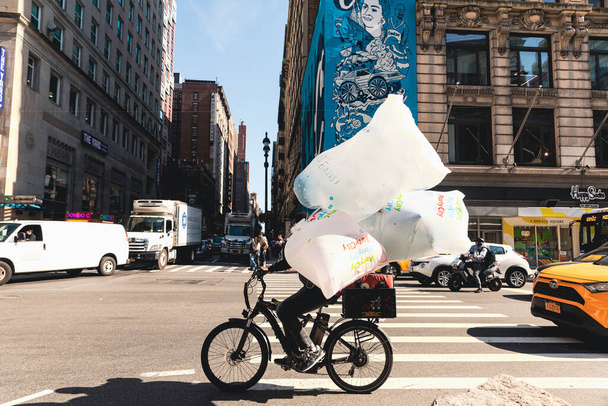 NEW YORK, USA - OCTOBER 13, 2022: delivery man with cellophane bags riding bicycle on crossroads of city street - Fotoğraf, Görsel