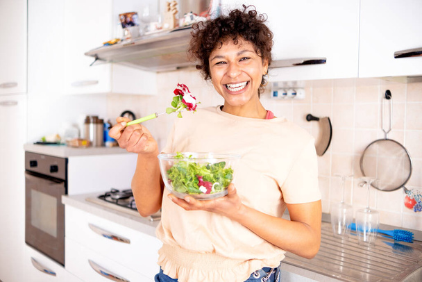 Cheerful black woman eating salad at home ready for diet - Fotoğraf, Görsel