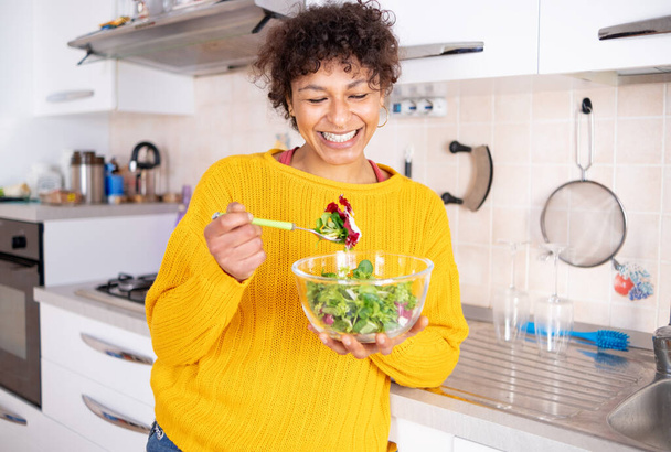 Cheerful black woman eating salad at home ready for diet - Foto, immagini