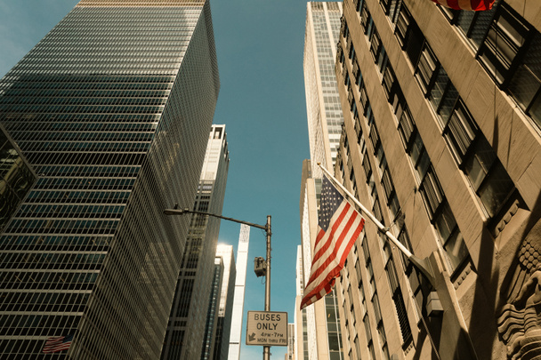 vista en ángulo bajo de la bandera de EE.UU. y la señal de tráfico cerca de edificios modernos en la ciudad de Nueva York - Foto, imagen
