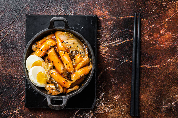 Korean Topokki or Tteokbokki rice cake with egg and mashrooms. Dark background. Top view. - Foto, Bild