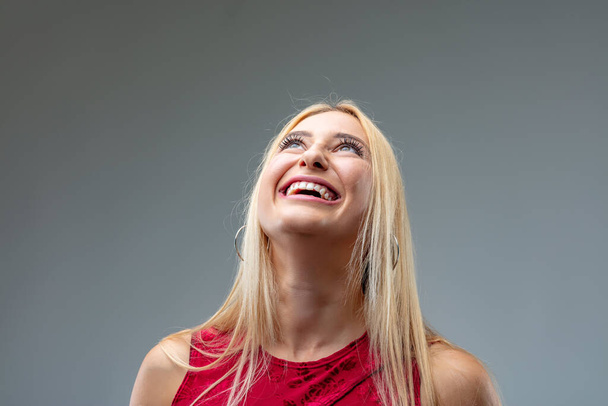 фронтальний портрет молодої блондинки в глибокій червоній сукні; поступово сміється все більше і більше, коли вона дивиться вгору і згинає голову назад і насолоджується
 - Фото, зображення