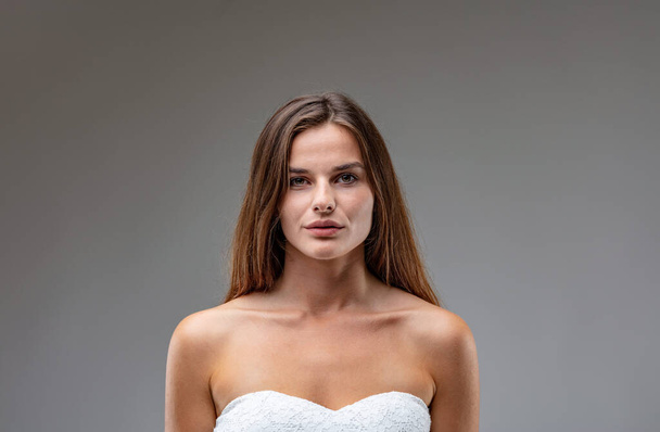 Central frontal portrait of charming and attractive young brown-haired woman wearing a white strapless dress. She conveys both the strength of beauty and youthful physique and that of willpower and in - 写真・画像