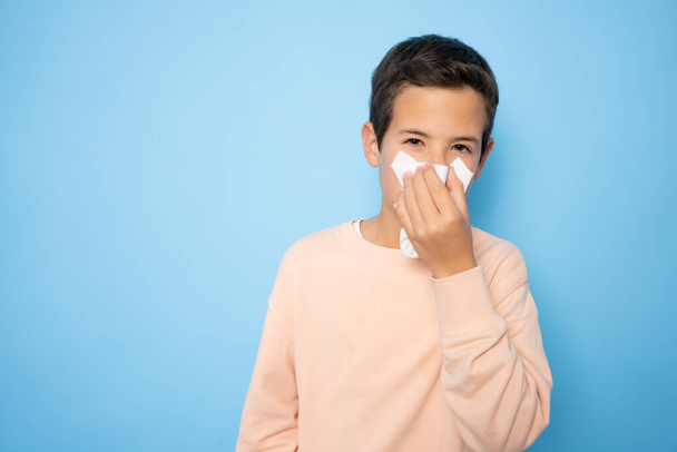 Kind mit laufender Nase pustet es in ein Papiertaschentuch. Grippe im Kindesalter. Gesundheit und medizinische Versorgung. - Foto, Bild