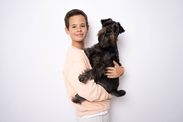 Dog Schnauzer and smiling boy hugs her with tenderness and look at camera on yellow background. Pets. Emotions of people. Childhood. Life style. Pet care. Copy space - Φωτογραφία, εικόνα