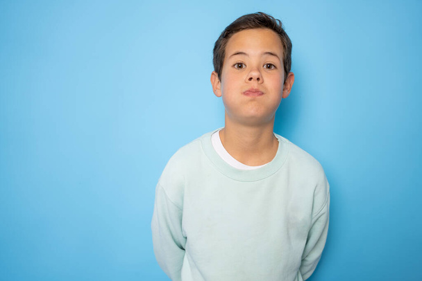 Beautiful kid boy wearing casual sweater standing over isolated blue background puffing cheeks with funny face. Mouth inflated with air, crazy expression. - Photo, image