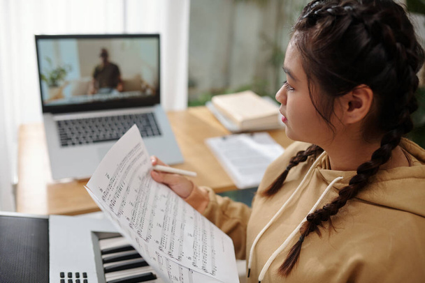 Teenage girl having online class with teacher explaining music notes in detail - Foto, afbeelding