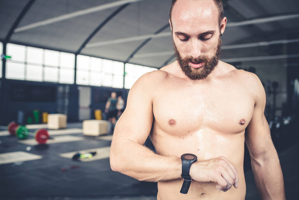 Αθλητικός νεαρός με έξυπνο ρολόι και smartphone σε εσωτερικούς χώρους γυμναστήριο μετά την προπόνηση - τεχνολογία, σπορ, fitness concept - Φωτογραφία, εικόνα