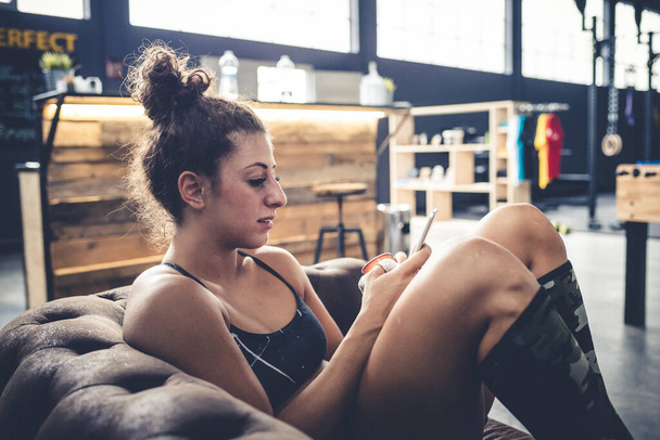 young woman sitting couch gym using smart phone after training  - sociable, internet, technology concept - Photo, Image