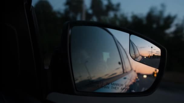 Reflectie van de zonsondergang in de achteruitkijkspiegel van een auto. Reizen met de auto. Achteruitkijkspiegels. - Video