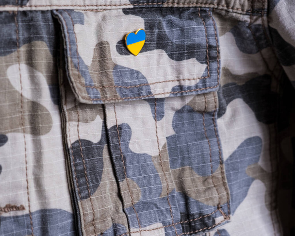 Metal badge with the flag of Ukraine in the shape of a heart on military jacket. Support for Ukraine. War in Ukraine. Ukraine flag theme - Foto, Imagem
