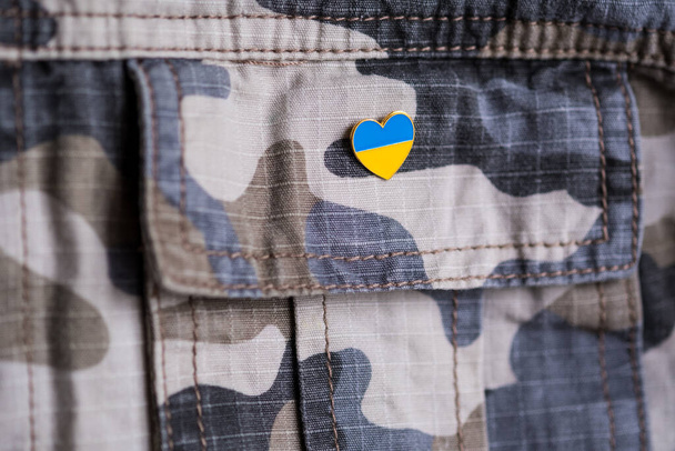 Metal badge with the flag of Ukraine in the shape of a heart on military jacket. Support for Ukraine. War in Ukraine. Ukraine flag theme - Photo, image