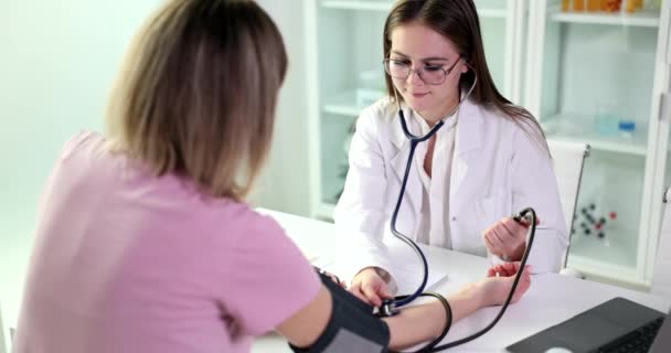 O médico que usa esfigmomanômetro com estetoscópio verifica a pressão arterial da mulher na clínica. Sinais e sintomas de pressão arterial elevada no ser humano - Filmagem, Vídeo