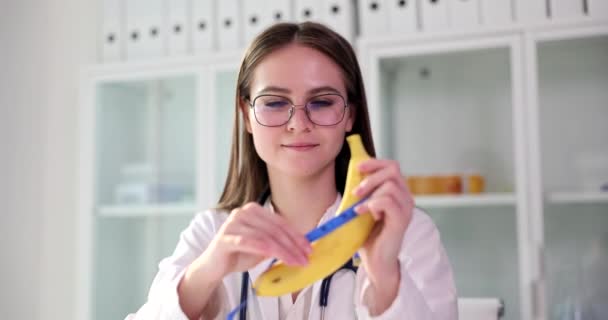 Doctor plastic surgeon holds a banana and measuring tape in hands. Penis enlargement concept - Πλάνα, βίντεο