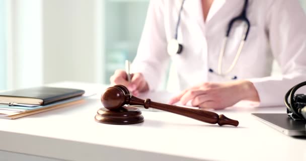 Soudní kladivo se stetoskopem na stole lékař píše poznámky v lékařském dokumentu. Lékařské právo a lékařské zločiny a úplatky - Záběry, video