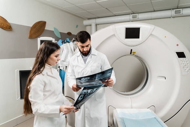 Kollegat lääkärit keskustelevat röntgenkuvat CT tietokonetomografia skannaushuone. Lääkäri harjoittelija tyttö opiskelee CT tietokonetomografia skannaus huone harjoittelujaksoja - Valokuva, kuva