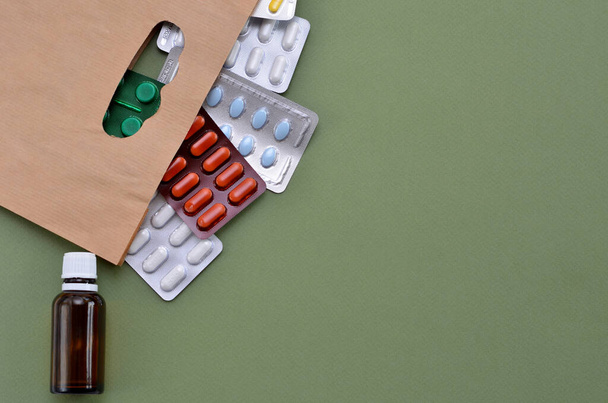 diferentes medicamentos, pastillas en una bolsa de papel sobre un fondo verde, espacio para copiar - Foto, imagen