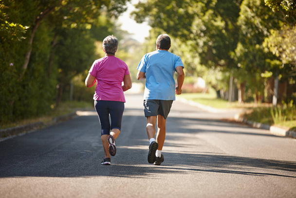 Motivándose mutuamente para mantenerse saludables. Vista trasera de una pareja madura corriendo juntos en un día soleado - Foto, imagen
