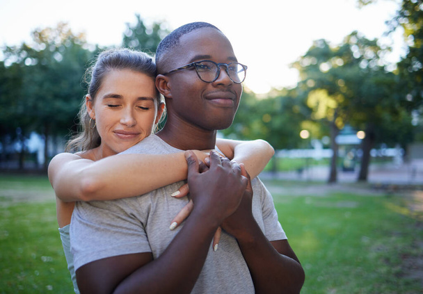 Love, peace or couple of friends hug in a park bonding on a relaxing romantic date in nature together. Interracial, young black man and happy woman embrace enjoying quality time on a holiday vacation. - 写真・画像