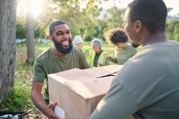 Community service, black man and giving box in park of donation, volunteering or social responsibility. Happy guy, NGO workers and helping with package outdoor of charity, support or society outreach. - Foto, imagen
